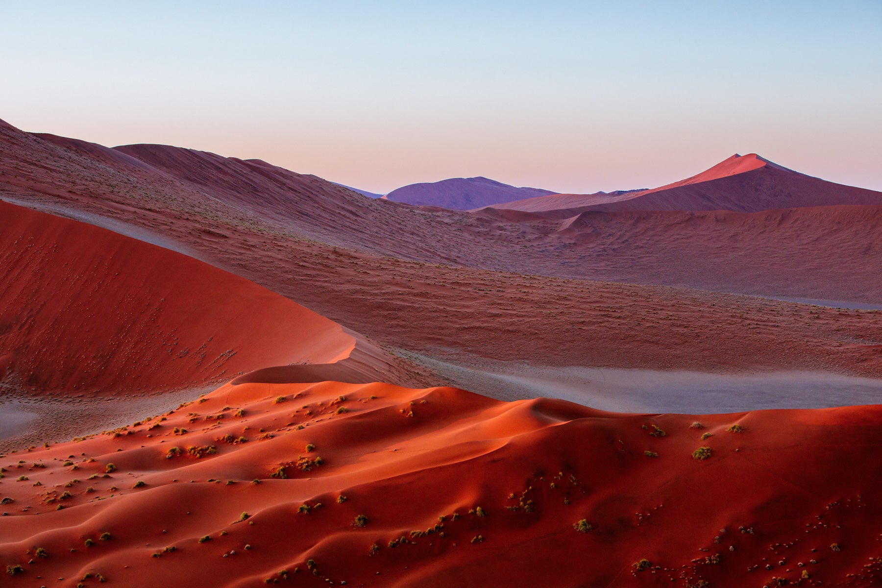 Aerial photograph of deep red sand dunes in Namibia at sunrise with soft pastel sky