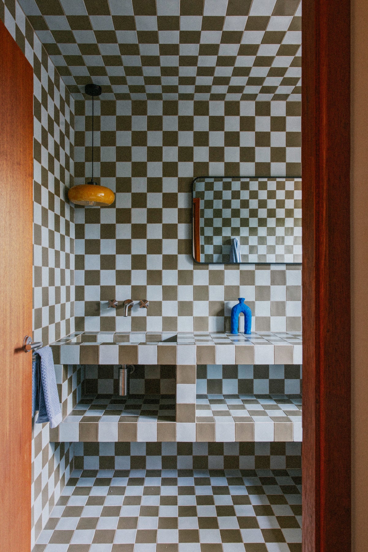 Checkerboard-tiled bathroom with yellow pendant light and blue vase on counter