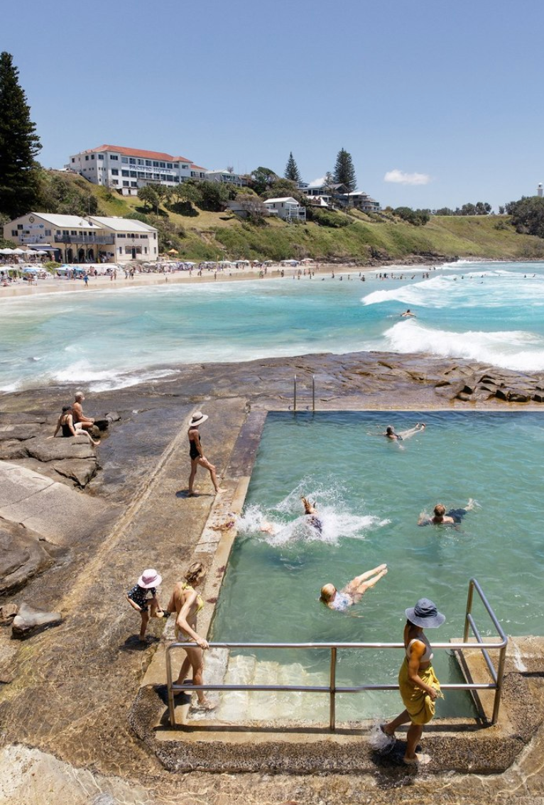 Swimmers enjoying Yamba’s ocean pool on a sunny day with surf, shoreline, and beachgoers in view