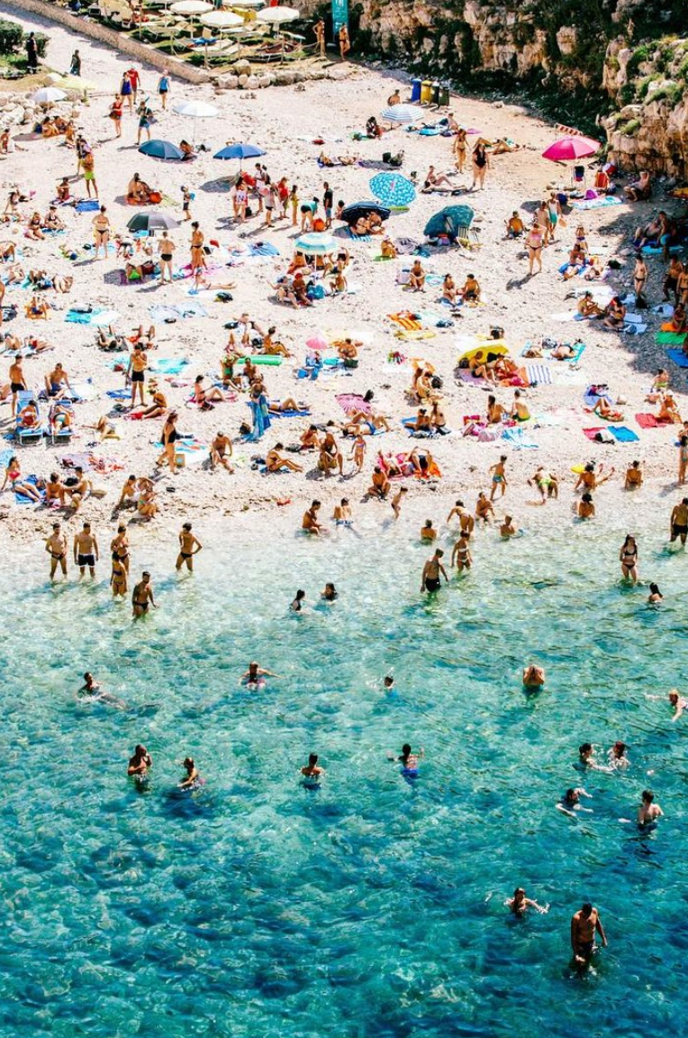 Aerial photo of people swimming and sunbathing on a pebbled beach in Polignano a Mare, Italy